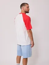 Remera blanca con mangas raglán negras y estampado frontal con el logo de Rusty en azul.