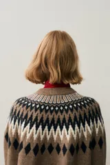 Buzo oversized de punto jacquard suave en color marrón, con cuello redondo y mangas raglán. Presenta un patrón geométrico en el pecho y los puños en tonos blanco y azul marino. Remates acanalados en cuello, puños y bajo.