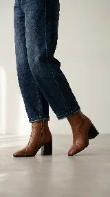 Bota de caña media confeccionada en cuero negro, con diseño de líneas simples, punta cuadrada y taco cuadrado firme.