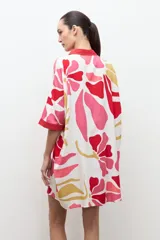 Túnica de corte recto y suelto con estampa floral en tonos de rosado, rojo y amarillo, cuello camisero rojo y mangas cortas holgadas.