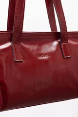 Cartera mini tote de cuero vacuno color bordó, con acabado charol, doble asa de mano y estructura rígida.