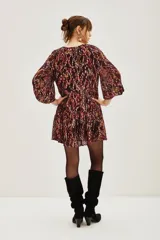 Vestido corto de jacquard con estampado ikat en tonos bordó y detalles metalizados. Presenta mangas largas abullonadas, escote en V con lazo y falda con volados.