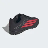 Championes de fútbol Adidas F50 Club para césped artificial, color negro con detalles en rojo y blanco. Presentan un exterior sintético liviano, lengüeta transpirable y suela de caucho con tapones diseñados para un agarre óptimo en canchas artificiales.