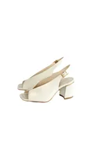 Zapato destalonado de cuero natural color off-white, con taco cuadrado alto, punta cuadrada y tira ajustable en el talón. Cuenta con una abertura en el empeine y detalle de ribete dorado en la parte superior del tacón.