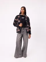 Campera reversible de diseño holgado, con un lado en tejido sherpa estampado con motivos florales en tonos negro y beige, y el otro lado en nylon negro. Cuenta con cierre frontal y cordones ajustables en el ruedo.