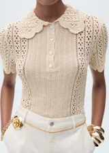 Jersey de punto calado en color beige, con diseño de manga corta, cuello polo con terminación en ondas y cierre frontal de botones.