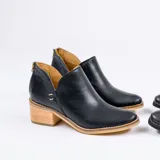 Botín de cuero vacuno color negro, con diseño de corte lateral, cierre metálico en el talón y taco foliado de madera en tono natural.