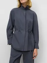 Camisa de algodón orgánico color gris oscuro, con cuello tipo tira, cierre frontal oculto con botones y manga larga. Presenta un diseño con cinturón fino integrado en la cintura para ajustar la silueta.
