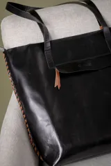Bolso tipo tote de cuero vacuno con textura de reptil, color marrón. Presenta detalles de pasamanería en los bordes laterales y una borla de flecos de cuero colgante. Cuenta con cierre superior.