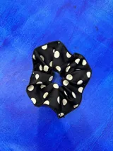 Colita de pelo tipo scrunchie de tela negra con estampado de lunares blancos.