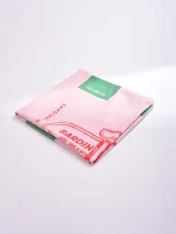 Pareo de tela, color rosa pálido, con estampado gráfico que simula una lata de sardinas en rojo y detalles en verde. Incluye un parche con el texto "Guapa!".