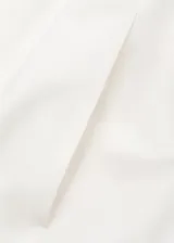 Vestido midi color blanco de diseño evasé y corte asimétrico con un hombro descubierto. Cuenta con un volante grande en el escote, detalles cut-out en la cintura y falda larga y amplia con bolsillos.