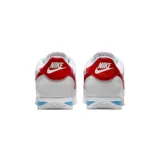 Championes Nike modelo Cortez, de diseño clásico en color blanco con el logo de la marca en rojo vibrante en los laterales y talón. Presenta una entresuela con una franja azul distintiva y suela dentada para mayor tracción.