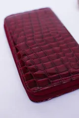 Billetera rectangular con cierre perimetral, confeccionada en cuero con textura de reptil. Cuenta con múltiples compartimentos internos para tarjetas, documentos y billetes, además de un bolsillo interior con cierre para monedas.