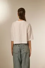 Remera blanca de corte holgado con mangas 3/4 y cuello redondo a la base. Presenta un diseño con apliques de studs metálicos distribuidos por toda la prenda.