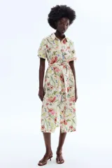 Vestido midi de corte camisero con estampado floral multicolor sobre base beige, cuello camisero, botonadura frontal completa, mangas cortas con lazo y cinturón del mismo género para ajustar en la cintura.