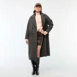 Abrigo largo de mujer, estilo lanoso, con estampado de pata de gallo o príncipe de Gales en tonos grises y marrones. Presenta un corte recto y holgado, cuello con solapas anchas y cierre cruzado con doble botonadura oscura.