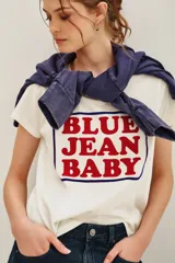 Remera de algodón color blanco con estampa frontal en letras rojas que dice 'BLUE JEAN BABY' dentro de un recuadro azul. Posee cuello redondo y mangas cortas.