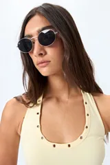 Top halter color crema con escote redondeado y detalle de ojales metálicos plateados alrededor del cuello. Diseño ajustado al cuerpo con espalda descubierta.