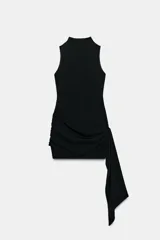 Vestido corto negro de cuello subido y sin mangas, con detalle de fajín drapeado en la cintura y caída lateral asimétrica.