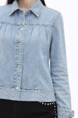 Campera de jean en tono celeste claro, con diseño de frunces en la parte superior delantera, mangas largas con puños ajustados y cierre frontal mediante botones metálicos.