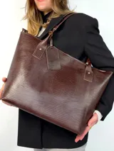 Cartera tipo tote de cuero genuino color marrón oscuro con textura de reptil. Cuenta con doble asa de hombro, cierre superior y un dije colgante de cuero a tono.