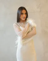 Vestido corto de red con acabado brillante, manga larga y detalle de plumas blancas en los puños. Presenta un diseño ajustado con escote redondo.