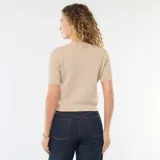 Sweater de punto en color beige, de manga corta y corte ajustado. Presenta un escote en V y cierre frontal con botones decorativos dorados en forma de concha.