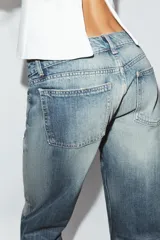 Jeans de tiro bajo y cinco bolsillos, con diseño de pierna ancha y larga. Presenta roturas y desgastes sutiles en la parte delantera. Cierre frontal con cremallera y botón metálico.
