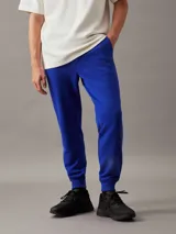 Pantalón de chándal azul eléctrico de felpa de algodón regenerativo, con cintura elástica con cordón, puños de canalé, bolsillos laterales y trasero, y logo de Calvin Klein en relieve en la cadera.