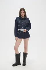 Campera de jean azul oscuro con costuras en contraste, corte cropped, cuello camisero, bolsillos frontales con solapa y cierre de botones metálicos.