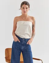 Top strapless de color beige, con diseño liso y ajuste al cuerpo. Cuenta con forro interno con elástico en el busto para mayor sujeción y pequeños tajos laterales en el ruedo.