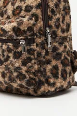 Mochila compacta con estampado animal print de textura suave y esponjosa. Cuenta con un bolsillo frontal con cierre, correas ajustables y asa superior en color marrón.
