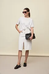 Falda midi de jean color negro, de corte recto con abertura central en la parte delantera, bolsillos y cierre con botón metálico.