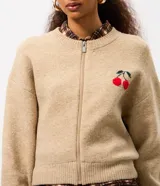 Cardigan de punto color beige con cierre frontal, cuello redondo, mangas largas y detalle bordado de cerezas en el pecho. Presenta puños y ruedo acanalados.