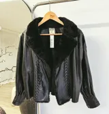 Chaqueta de cuero sintético negro con cuello de piel sintética, diseño de costuras trenzadas verticales en el frente y mangas con puños estructurados.