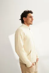 Campera tejida color marrón claro con cierre delantero, cuello alto y bolsillos delanteros. Tejida en 100% lana fina sin teñir.