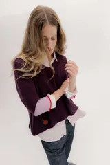 Buzo de punto en color negro con mangas tres cuartos y puños en contraste color marrón. Presenta un diseño holgado con tajos laterales y un aplique circular con logo en la parte inferior.