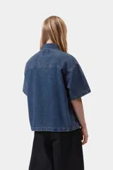 Camisa de denim de algodón celeste, de corte holgado y mangas cortas, con cierre frontal de botones metálicos y un bolsillo aplicado en el pecho con etiqueta de la marca.