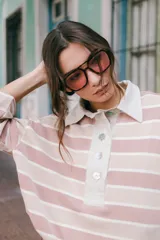 Remera tipo polo de tejido de punto a rayas horizontales en tonos rosados y beige. Presenta cuello camisero de lino, cierre frontal con botones de nácar y silueta holgada.