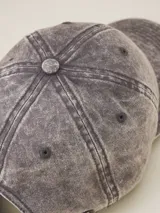 Gorra de béisbol color gris oscuro con efecto lavado o acid wash, visera curva y panel frontal estructurado. Presenta una pequeña etiqueta negra cosida en el lateral trasero.