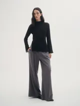 Blusa negra de crepe texturado, con cuello alto, mangas largas acampanadas y corte asimétrico con abertura lateral.