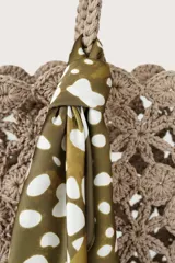 Pañuelo cuadrado de tela ligera con estampado orgánico de manchas blancas sobre fondo verde oliva. Presenta un borde ancho en tono verde oliva sólido con el nombre de la marca impreso en los extremos.