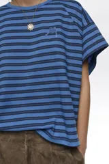 Remera corta de corte amplio confeccionada en 100% algodón, con diseño a rayas horizontales azules y negras, escote redondo, mangas cortas caídas y pequeño logo bordado en el pecho.
