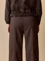 Pantalón de corte relajado color marrón, confeccionado en una mezcla de algodón y elastano. Presenta costuras en contraste color rojo en bolsillos y bragueta, con cierre de botón metálico.