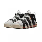 Championes Nike Air More Uptempo 96 de color blanco, negro y gris, con detalles en naranja y rojo. Presentan el característico diseño con las letras "AIR" sobredimensionadas en los laterales, suela de goma con amortiguación visible y un estilo urbano robusto.