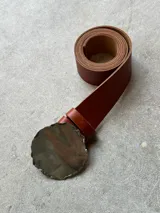Cinturón de cuero color marrón con hebilla dorada de forma irregular.