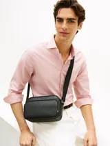 Bandolera Tommy Hilfiger de color negro, confeccionada en poliuretano con diseño de compartimento principal con cierre de cremallera y bolsillo exterior frontal con panel de textura tejida. Cuenta con correa ajustable, bolsillo interior con cierre y detalles distintivos de la marca con logo metálico en la parte delantera.