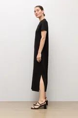 Vestido midi negro de manga corta y cuello redondo, con detalles de botones plateados en el hombro izquierdo, tajo lateral y un cinturón fino ajustable con hebilla metálica.