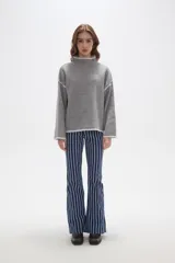 Polera de tejido de punto color negro con detalles de vivos en color beige en el cuello, puños, ruedo y costuras de las mangas. Presenta un diseño holgado con cuello alto y mangas largas.